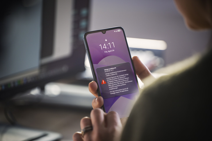 Närbild på hand som håller i en mobiltelefon. På skärmen syns ett varningsmeddelande.