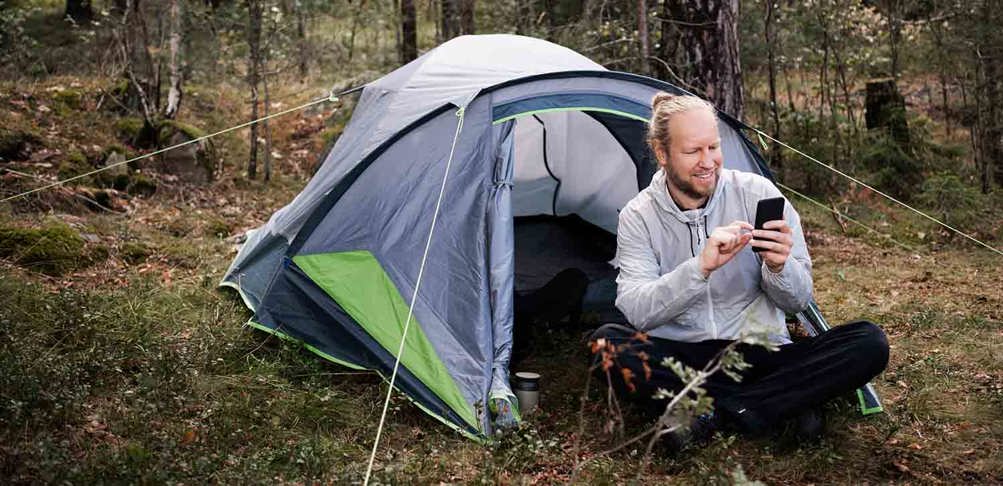 Person med mobil vid tält i skogen.