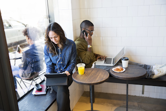 Två personer arbetar med telefon och dator på café.