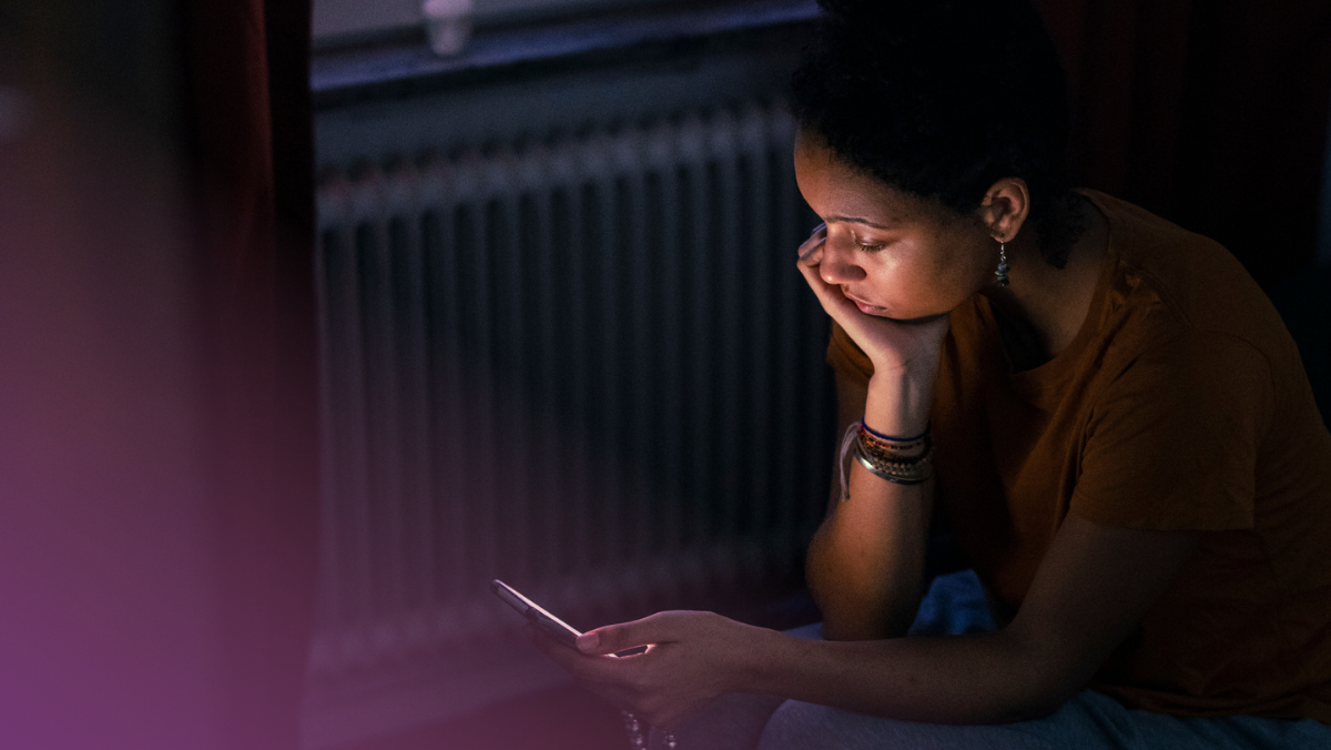 Person sitter i ett mörkt rum och tittar på mobiltelefon.