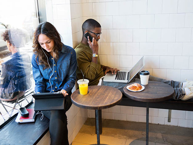 En man och en kvinna på café med datorer och telefoner.