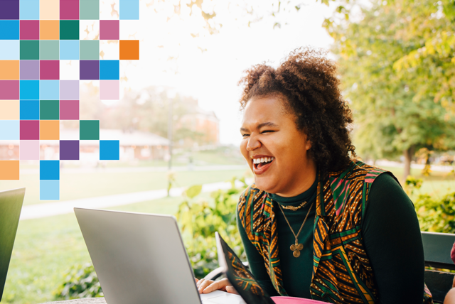 Glad person sitter framför dator utomhus i parkmiljö.