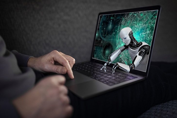 En person använder en bärbar dator med en skärm som visar en humanoid robot som sträcker ut händerna ut från skärmen mot tangentbordet.