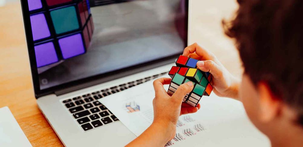 Person sitter framför en bärbar dator med en Rubiks kub i händerna.